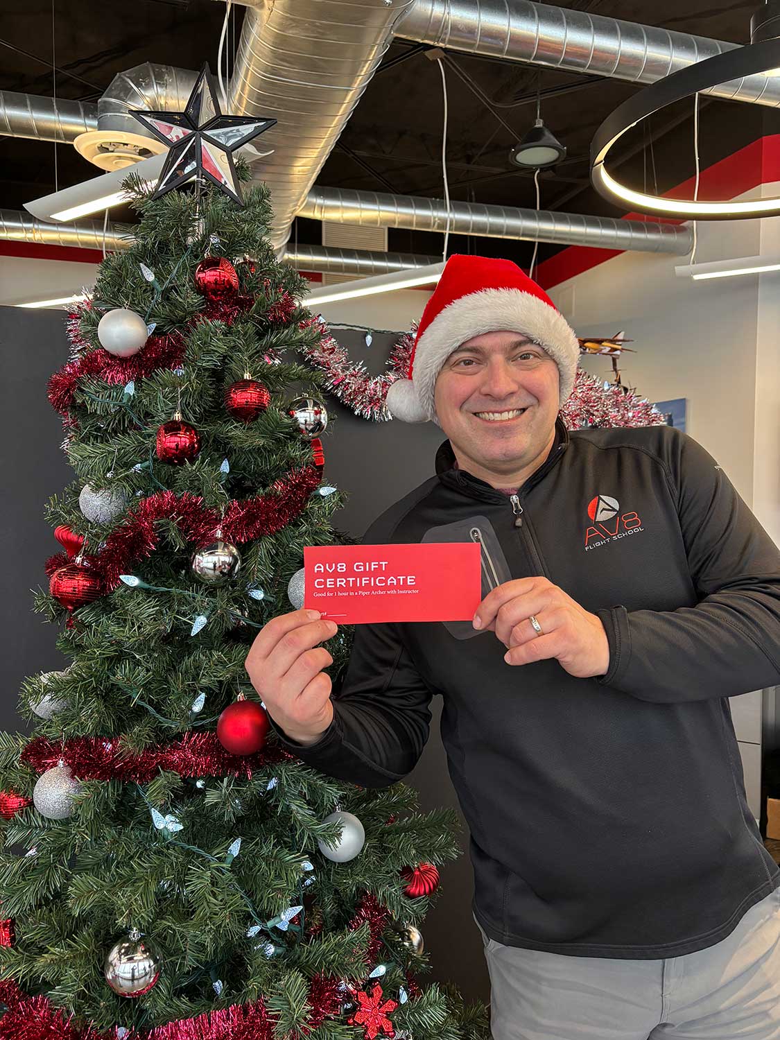 Gifts-for-Aviators-AV8 NIck in Santa Hat with AV8 Gift Certificate and holiday tree